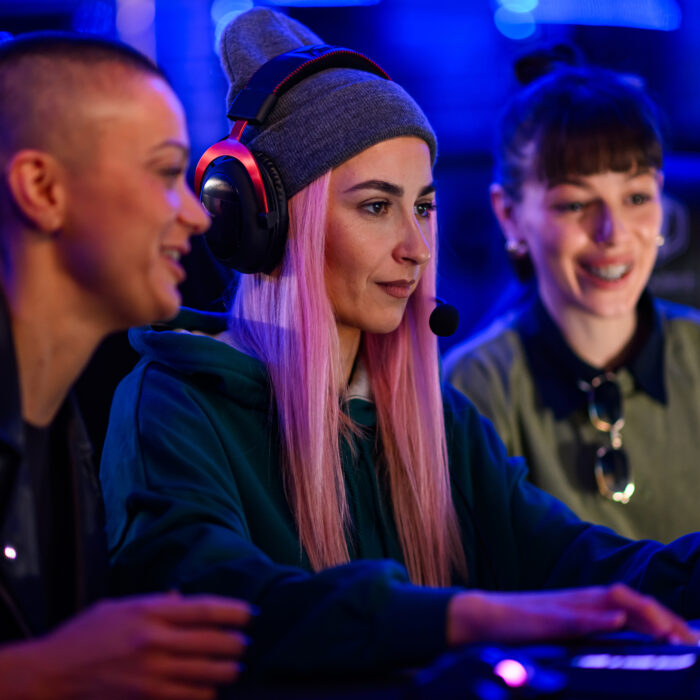 Young female gamer with a beanie cap playing PC video game and having fun with her friends. Video game player participating on a cybersport tournament in a Esports arena or on a Gaming convention.